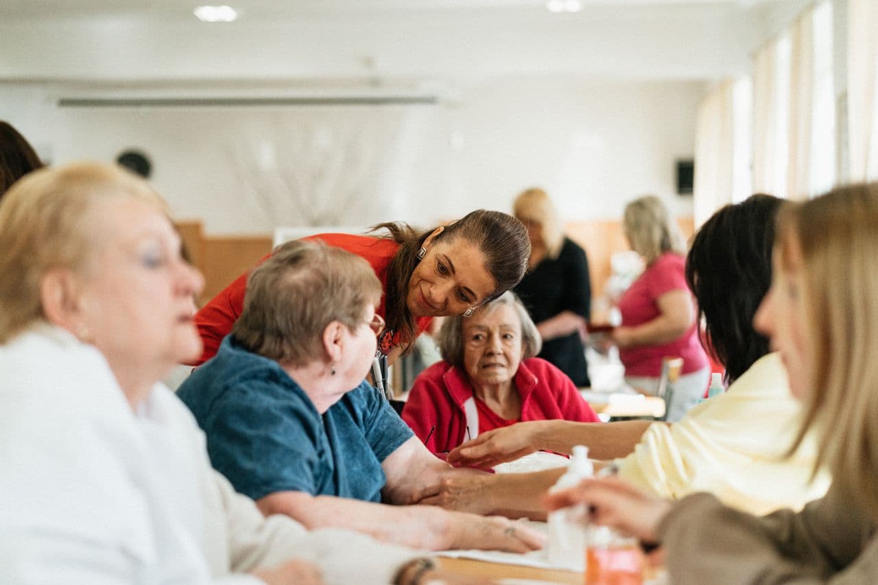 Care worker leaning in to help older women during a group table activity